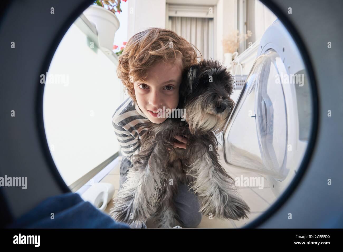 View From Inside Of Washing Machine Of Cute Curly Haired Child In Casual Wear Holding Small Dog And Looking With Interest Inside Stock Photo Alamy
