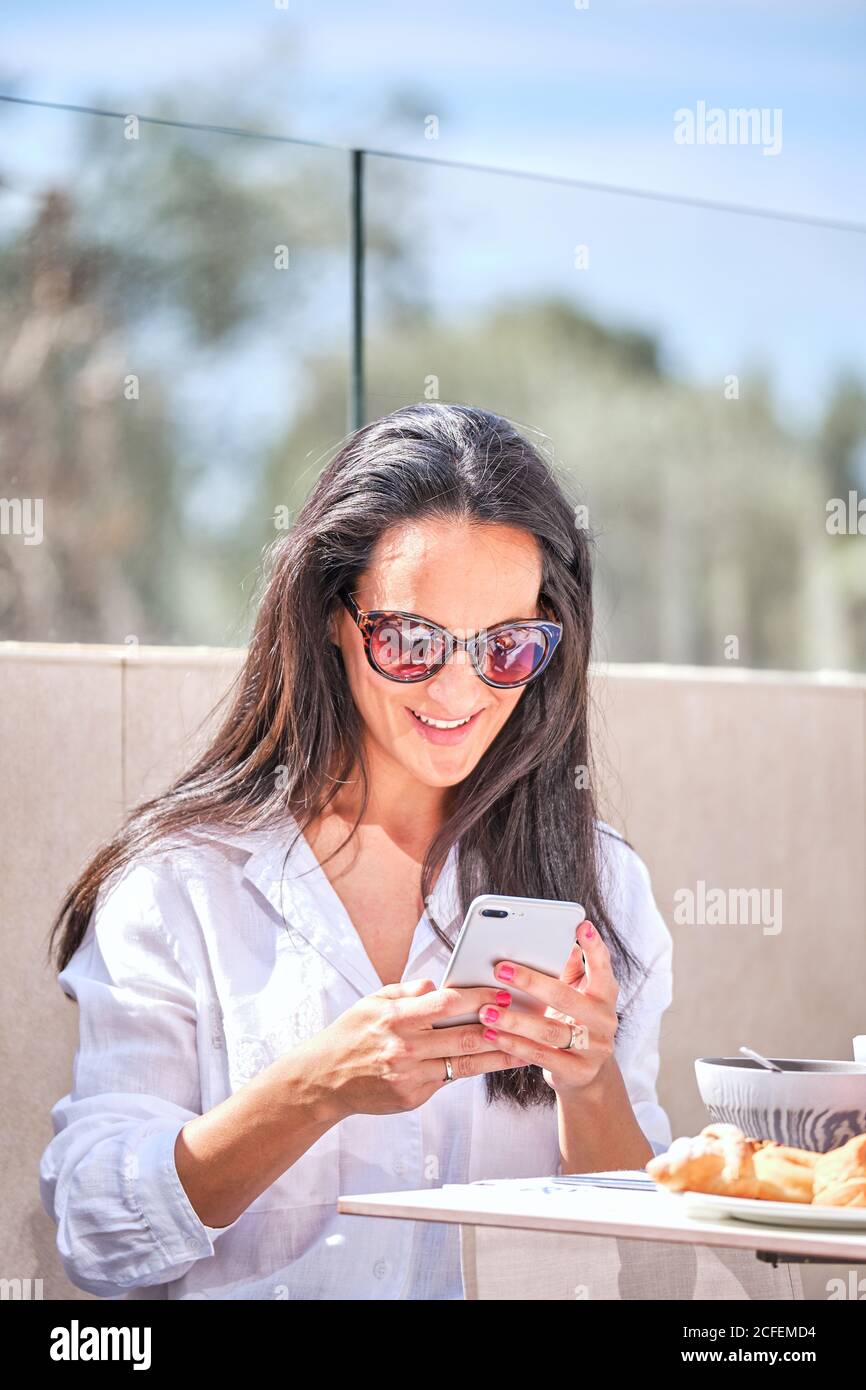 Smiling female blogger sitting at cafe at table with vegetable salad and taking picture of food with smartphone Stock Photo