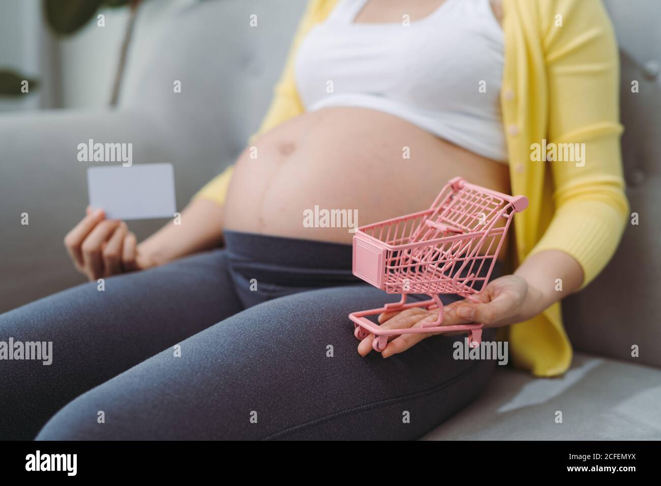 Pregnant woman preparing to buy baby products before birth, Holding shopping cart and credit card in front of the belly, Stock Photo