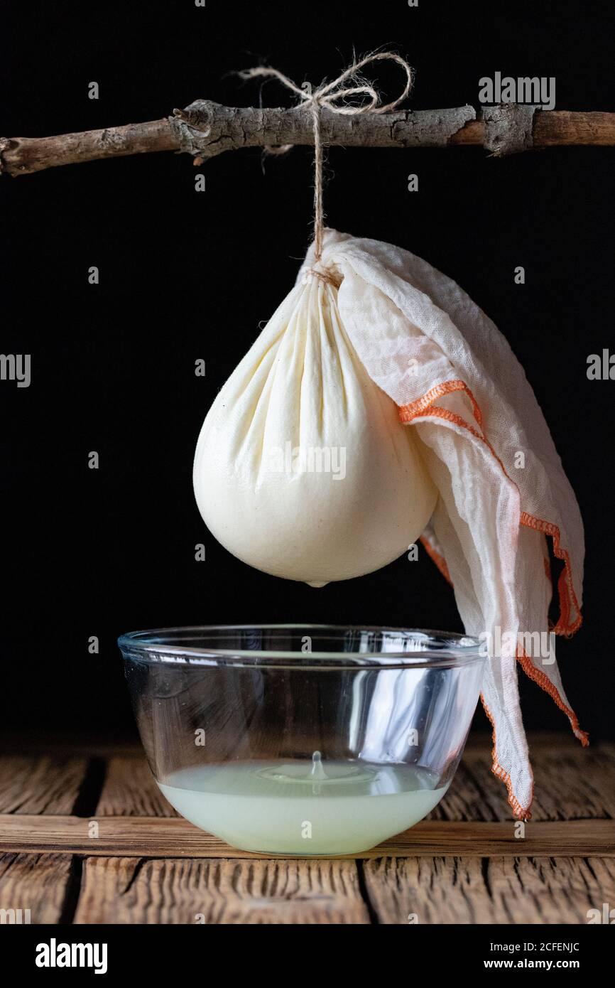 Cloth with ball of fresh labneh cheese hanging on twig over bowl with