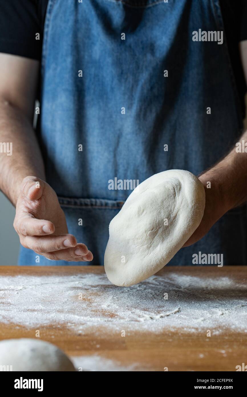 unrecognizable male in apron flattening soft dough over table with flour while cooking pizza Stock Photo