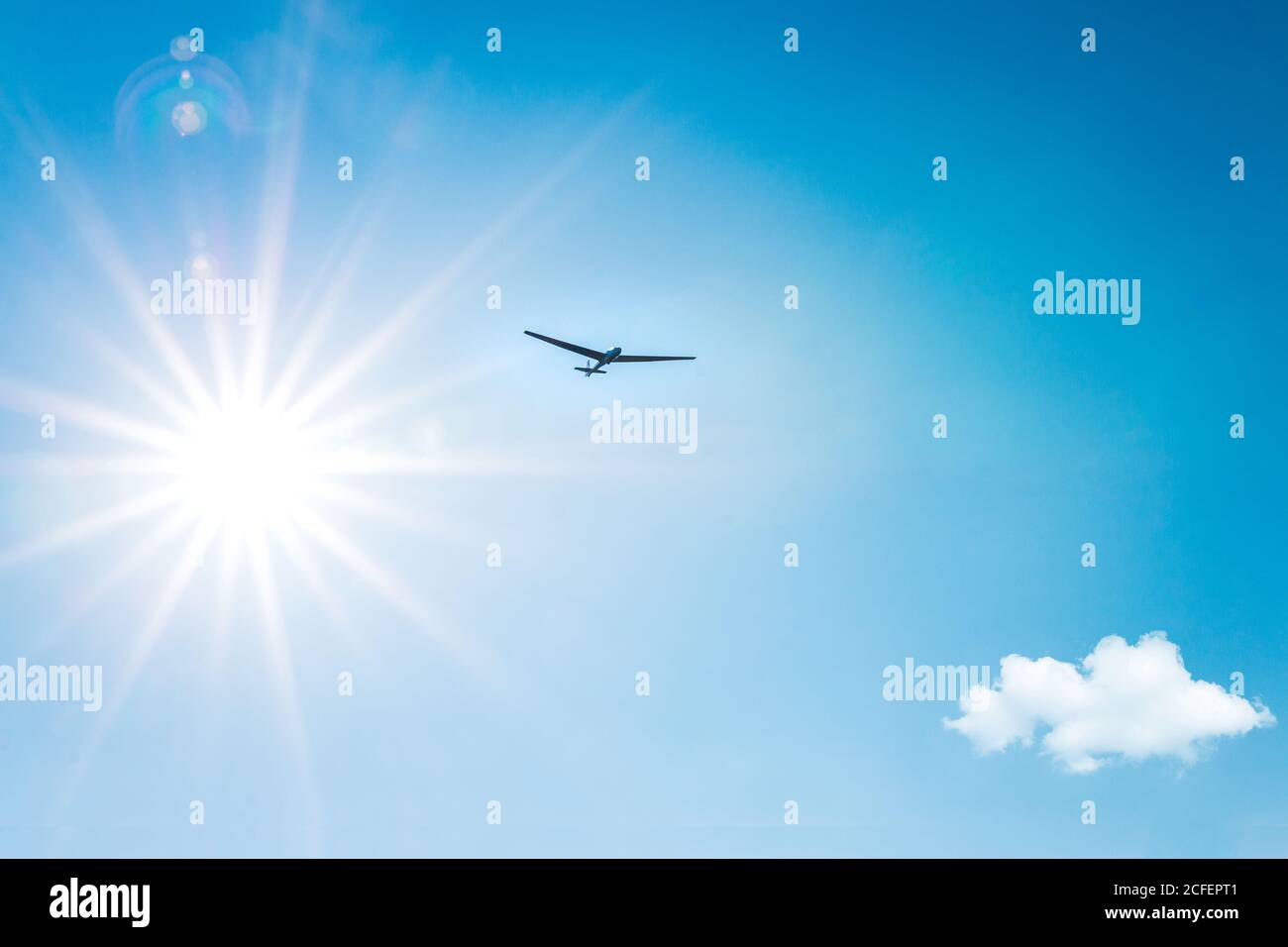 From below aircraft flying in blue sky near small cloud and vivid sun in Austria Stock Photo