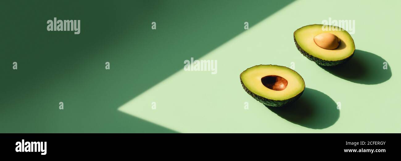 Avocado cut in half on a neo-mint background. Web banner with sunlight. Stock Photo
