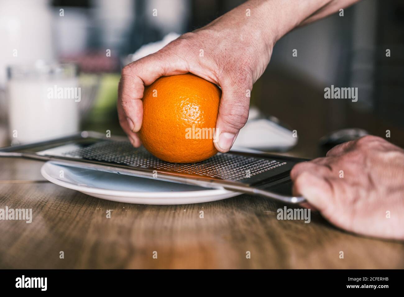 Side view of crop anonymous Woman removing orange zest with grater while preparing aromatic pastry in home kitchen Stock Photo