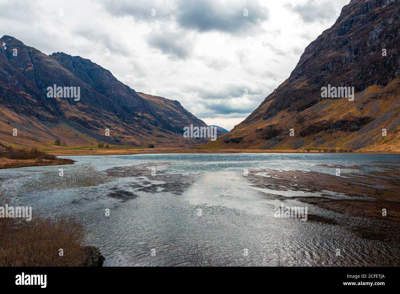 Amazing Scottish landscape of calm lake with mirrored surface reflecting mountain with snow covered peak and blue cloudy sky in Glen Coe area Stock Photo