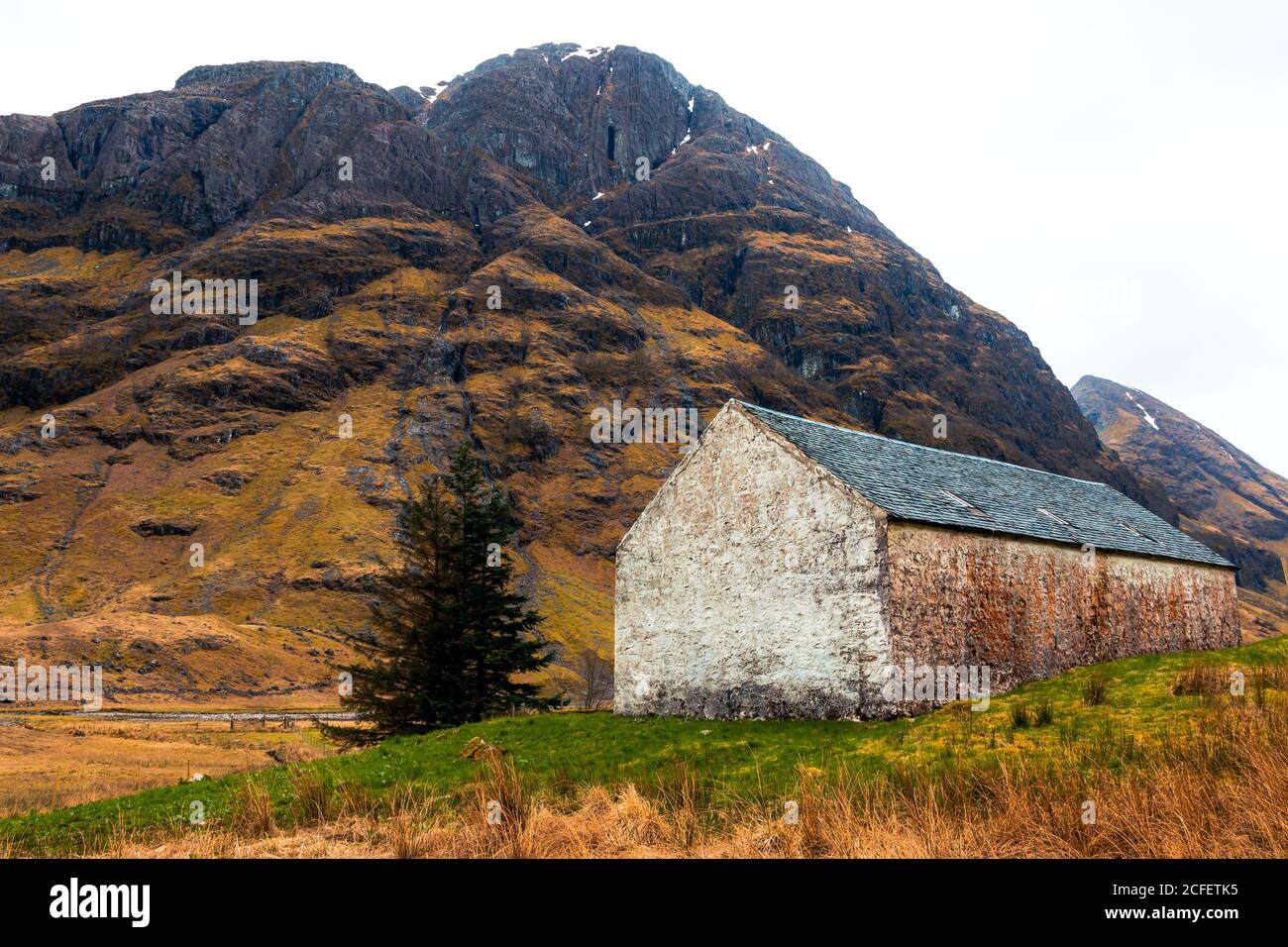 Aged stone house located on green hill against majestic rocky mountain in Scottish Highlands Stock Photo