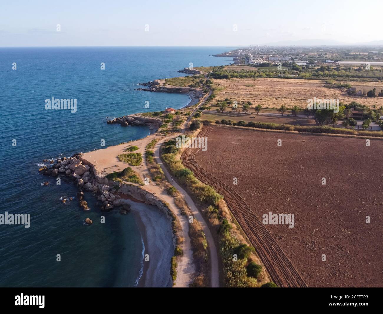 Aerial view of a rocky coastline near a plowed soil field at Jardi de Sol de Riu, Vinaros, Spain. Stock Photo