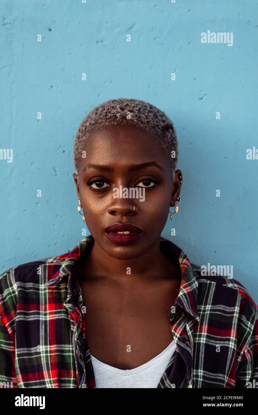Young African American female with short hair and piercing wearing black plaid shirt looking at camera with intense eyes and challenge while feeling sad Stock Photo