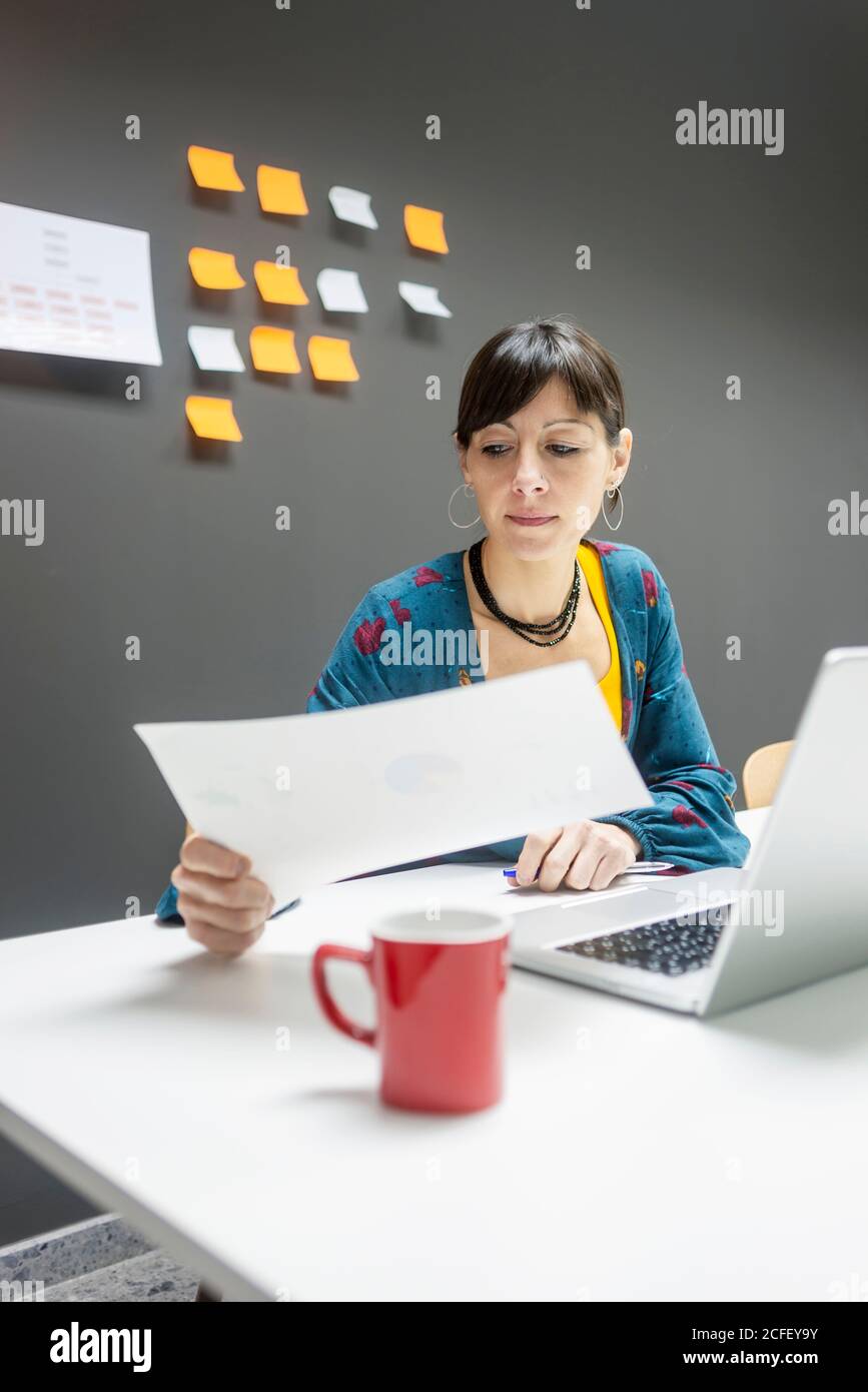 Pretty female working with documents while sitting at desk in modern office Stock Photo