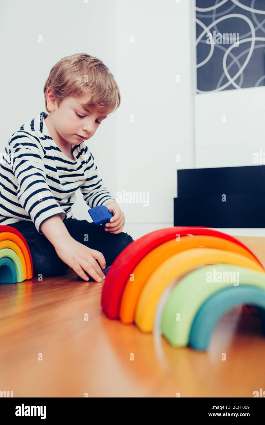 Blonde cute boy playing with waldorf rainbow puzzle Stock Photo