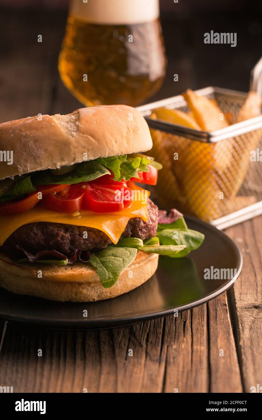 Homemade deluxe burger with cheese, lettuce, tomato and pickles on dark moody background Stock Photo