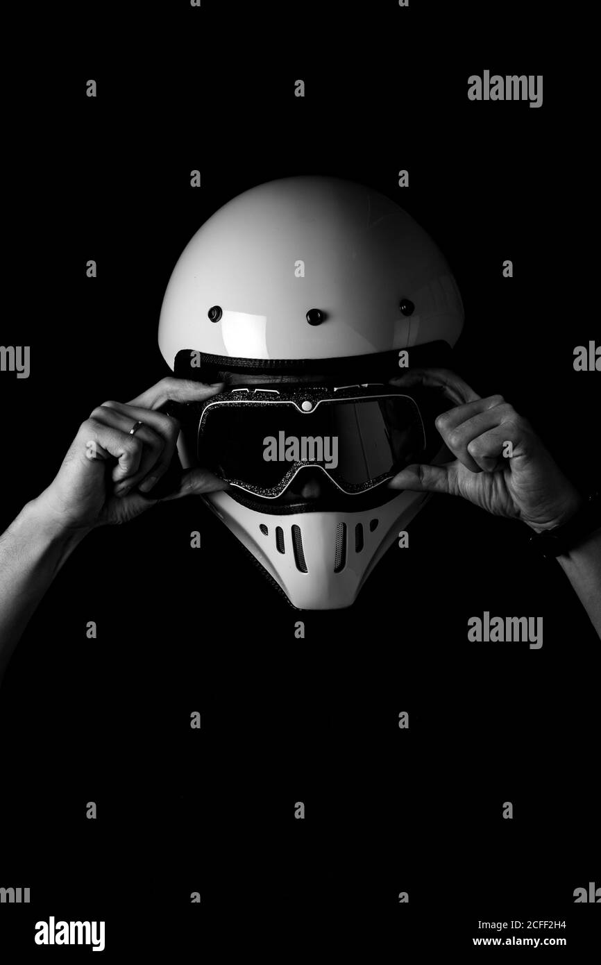 Black and white photo of faceless driver in helmet wearing black goggles and white helmet in studio Stock Photo