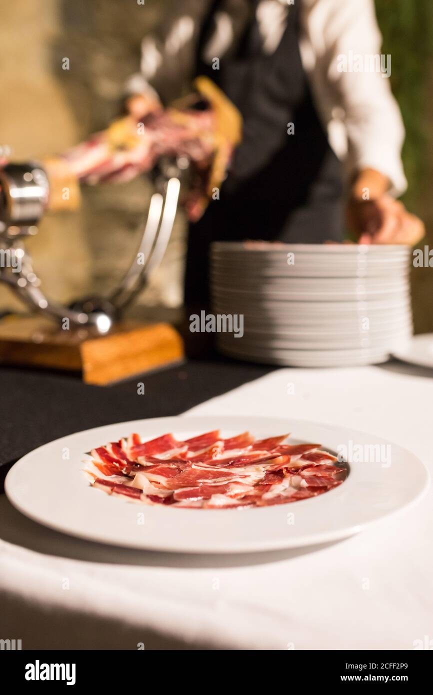 Crop unrecognizable person hand on apron cutting a whole drycured ham
