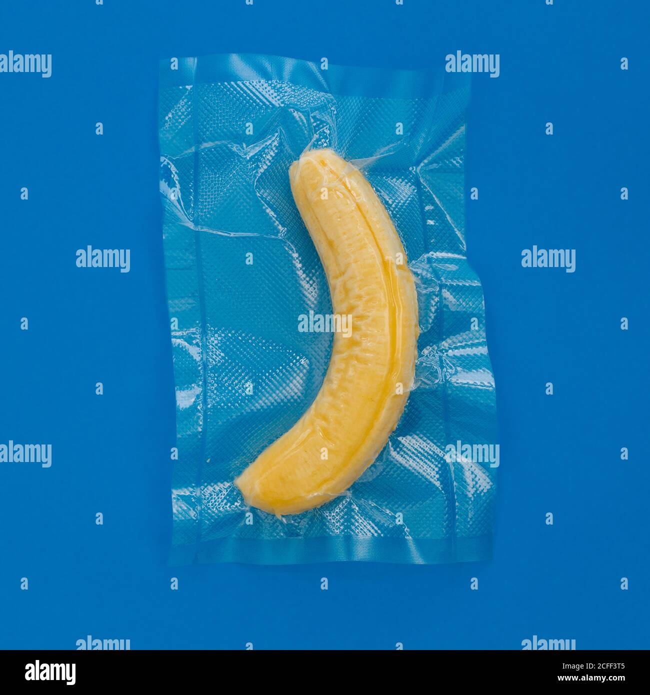 Top view of ripe yellow peeled banana in vacuum plastic bag on blue