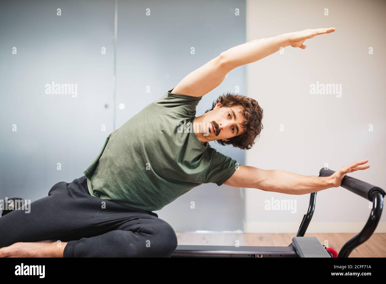 Focused male athlete in activewear sitting on pilates machine and doing ...