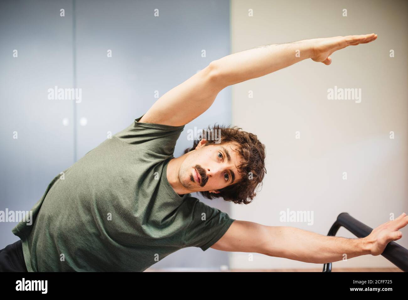 Focused male athlete in activewear sitting on pilates machine and doing ...