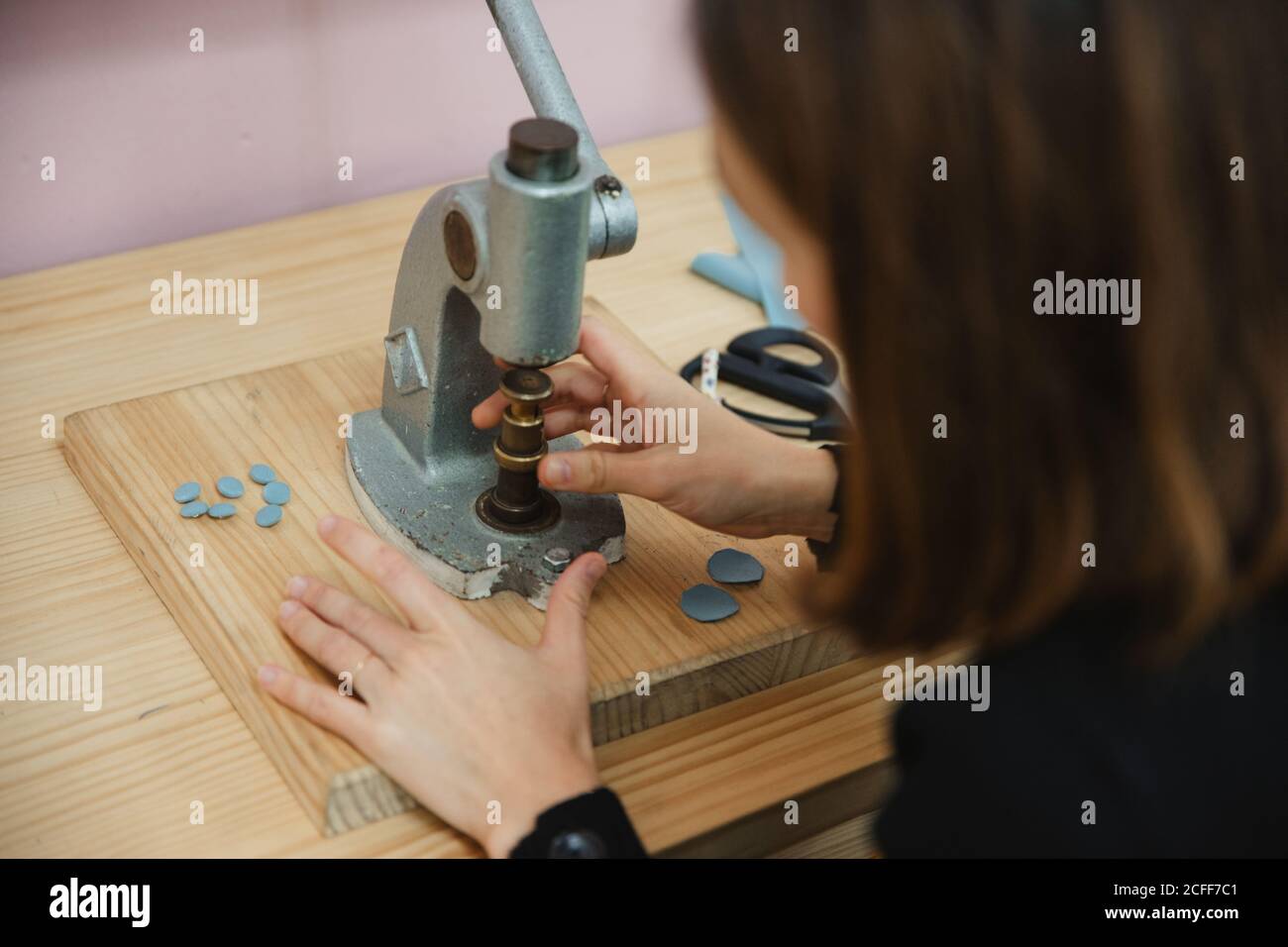 From above anonymous Woman using shabby button maker on workbench in tailor studio Stock Photo