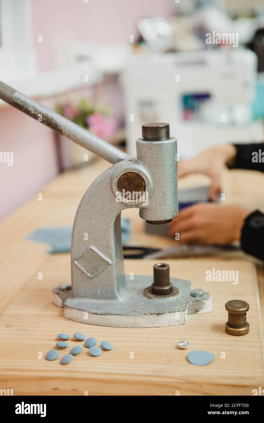 Crop anonymous person hands pulling lever of button maker on table in professional dressmaking workshop while making garment Stock Photo