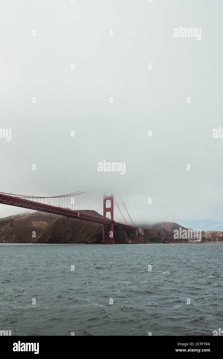 Powerful metal red bridge stretching from rocky shore above water in ...