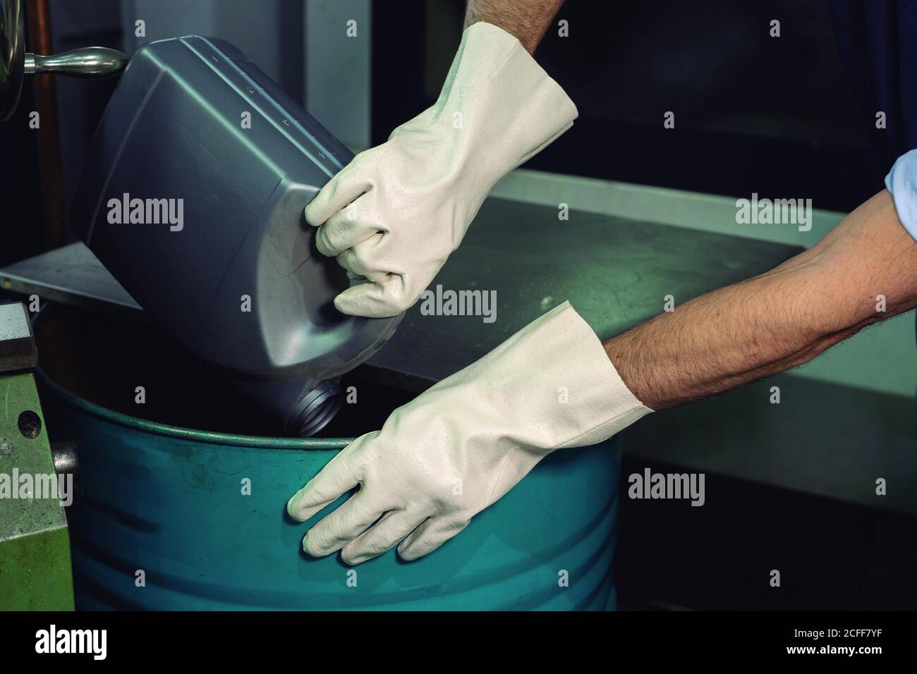 Crop unrecognizable foreman in gloves pouring chemical liquids from canister into metal  barrel in factory Stock Photo