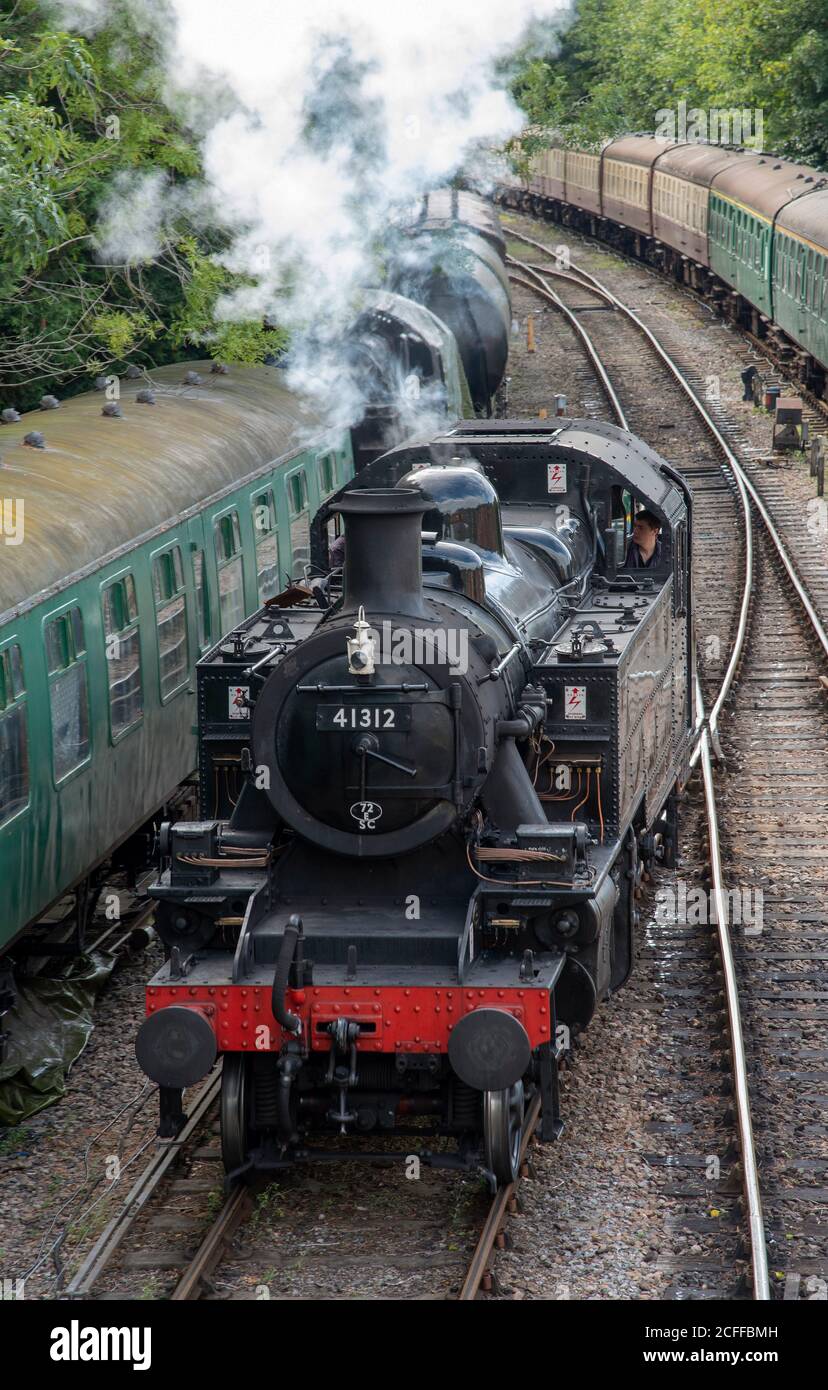 Alresford, Hampshire, England, UK. 2020. A steam tank engine approaching Alresford station passing rolling stock waiting to be renovated. Stock Photo