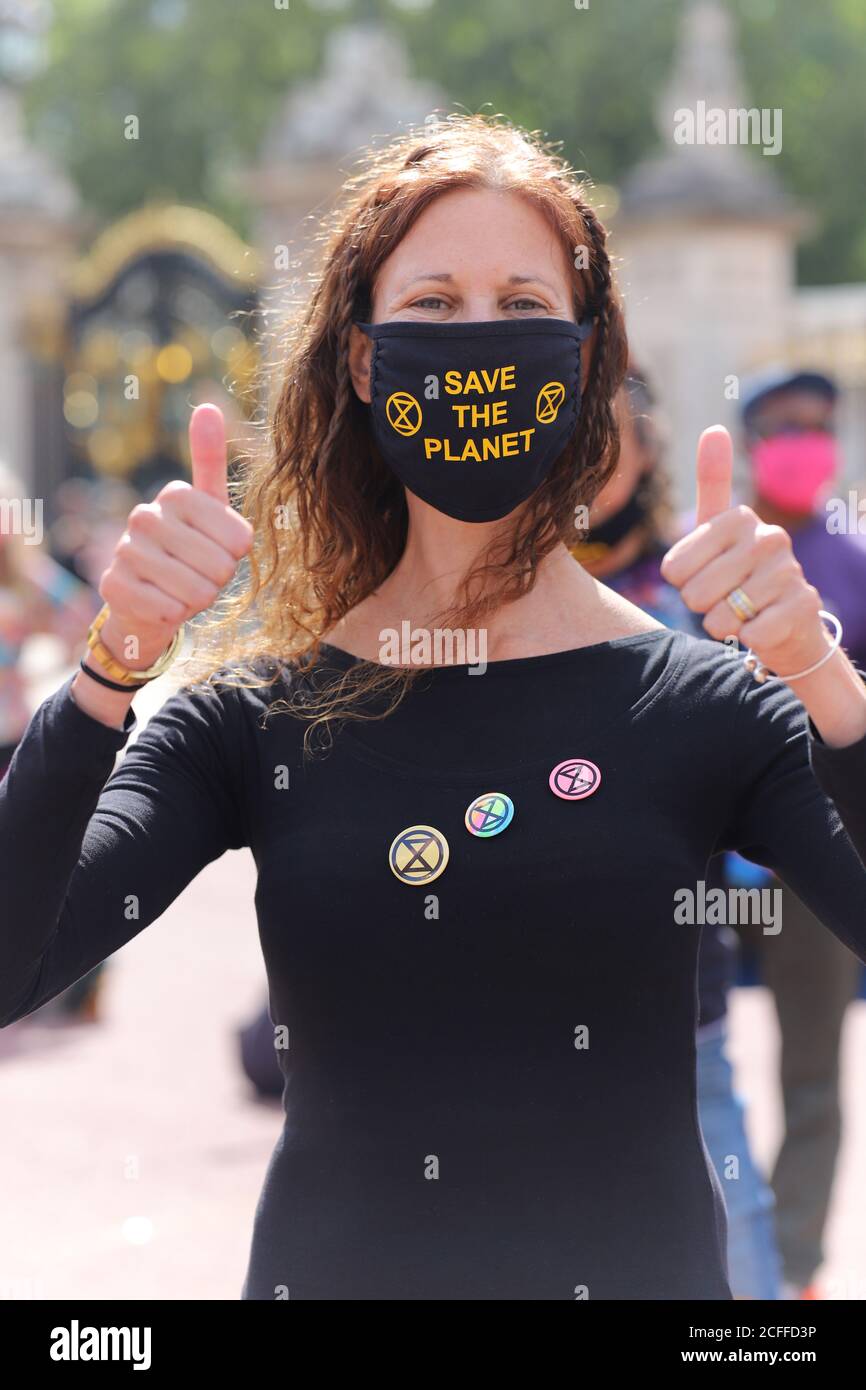 Extinction rebellion activists outside Buckingham Palace in London hold a discobedience dance off, 5th September 2020. A female protestor wears a face mask saying save the planet and XR badges Stock Photo