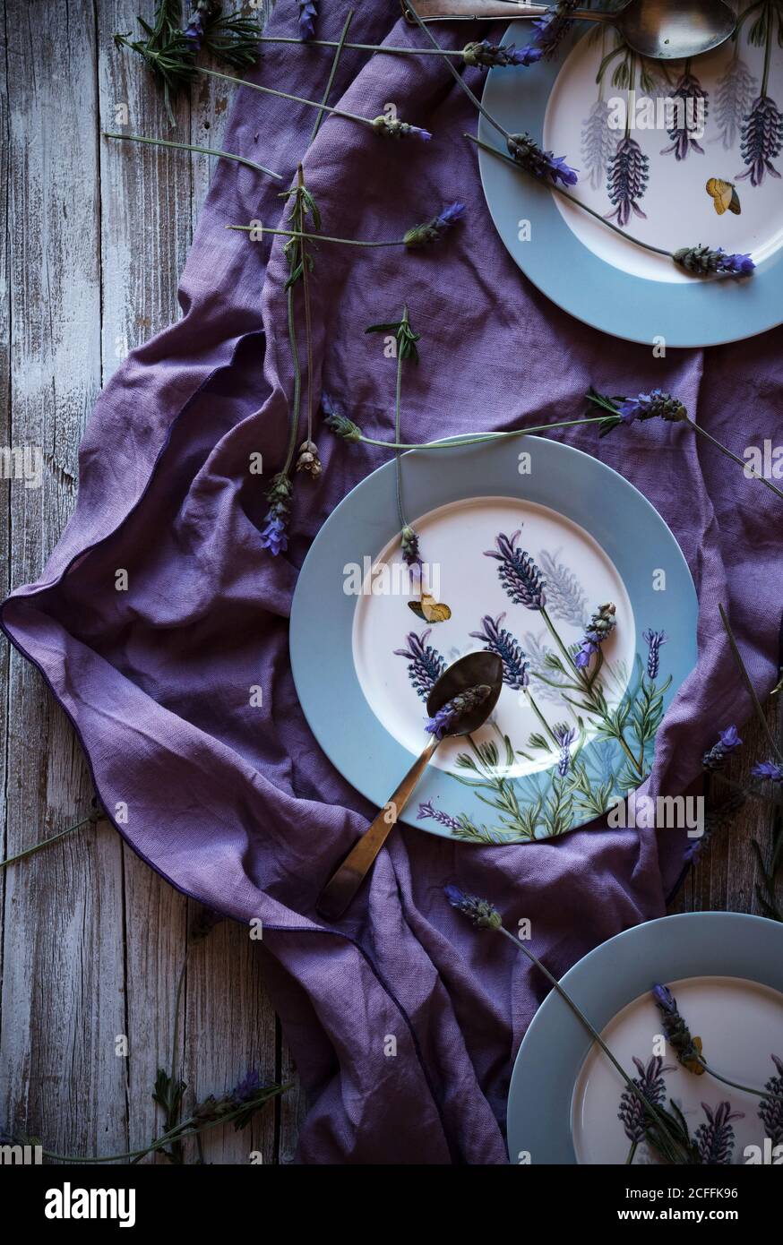 From above fresh lavenders placed around empty plates over violet fabric on lumber tabletop Stock Photo