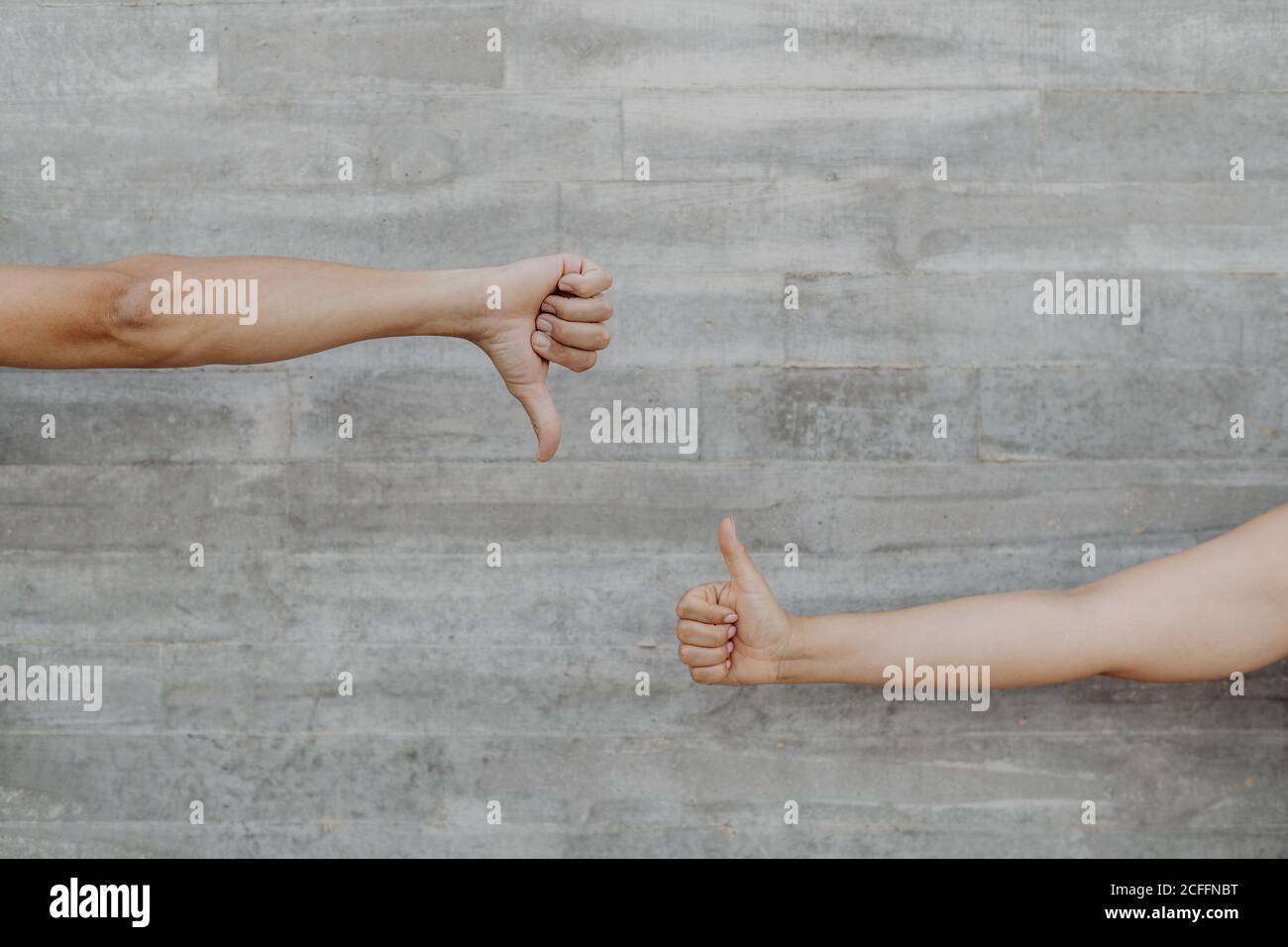 Tanned strong hands of crop man and Woman gesturing and showing thumb up and down on background of grey wall Stock Photo