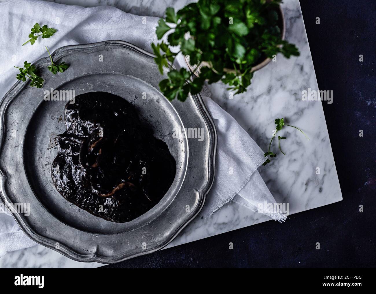 Top view of metal plate with plum jelly placed on white fabric on table together with bunch of parsley Stock Photo