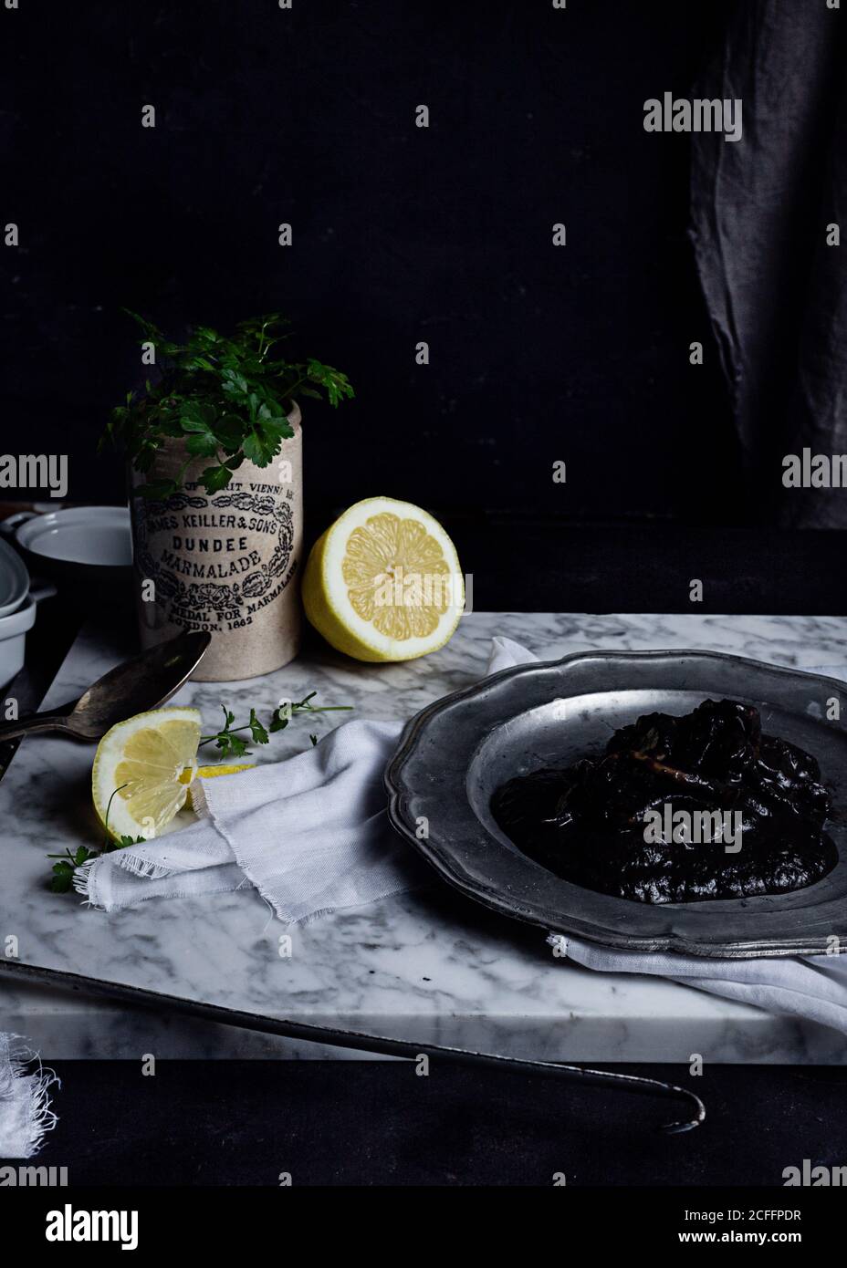 Metal plate with plum jelly placed on white fabric on table together with lime slices and bunch of parsley Stock Photo