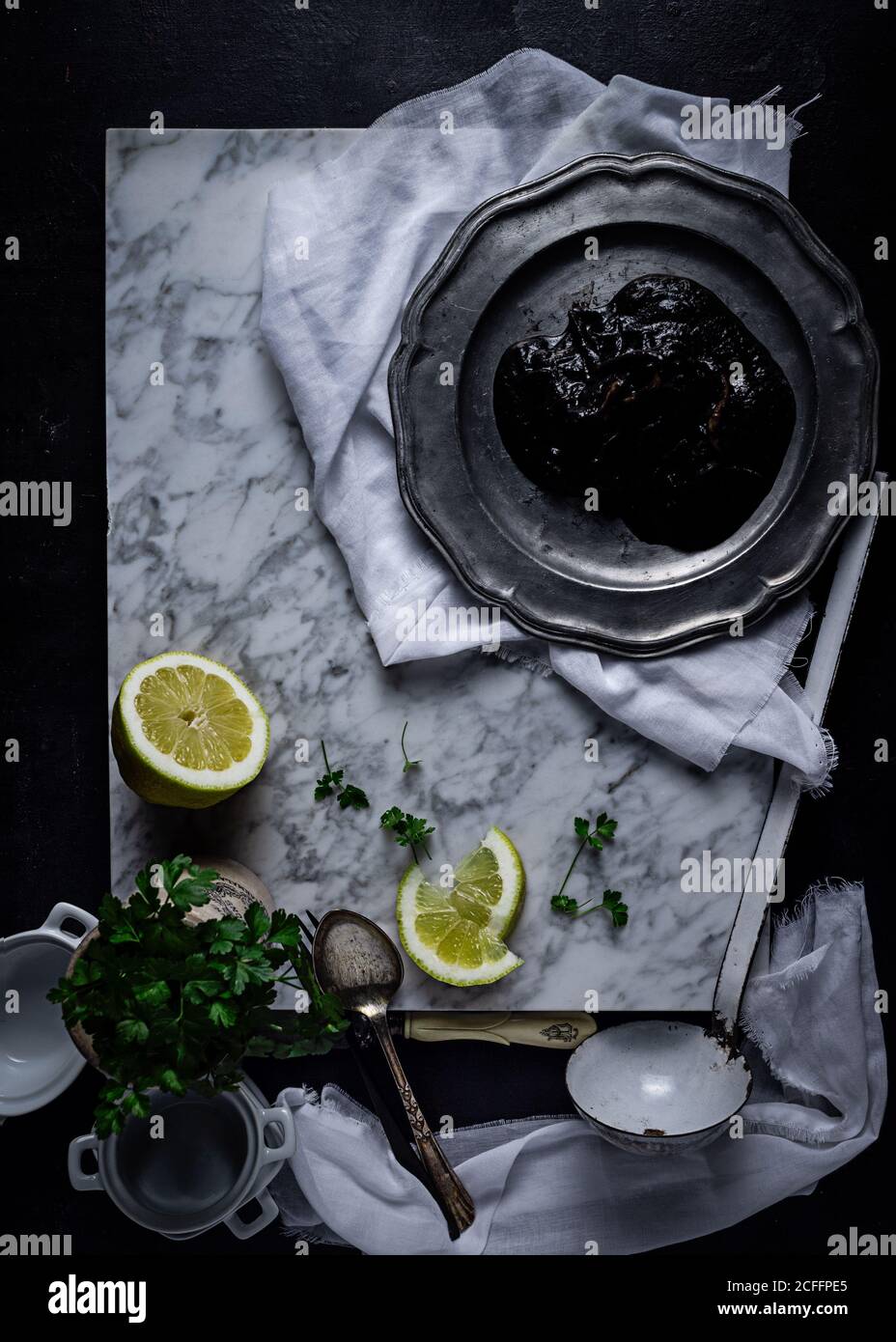 Top view of metal plate with plum jelly placed on white fabric on table together with lime slices and bunch of parsley Stock Photo