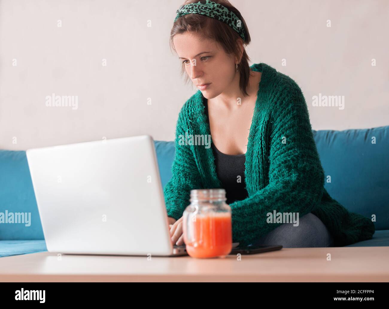 From below of female freelancer sitting in living room at table with a fresh juice while working online on project with her netbook Stock Photo
