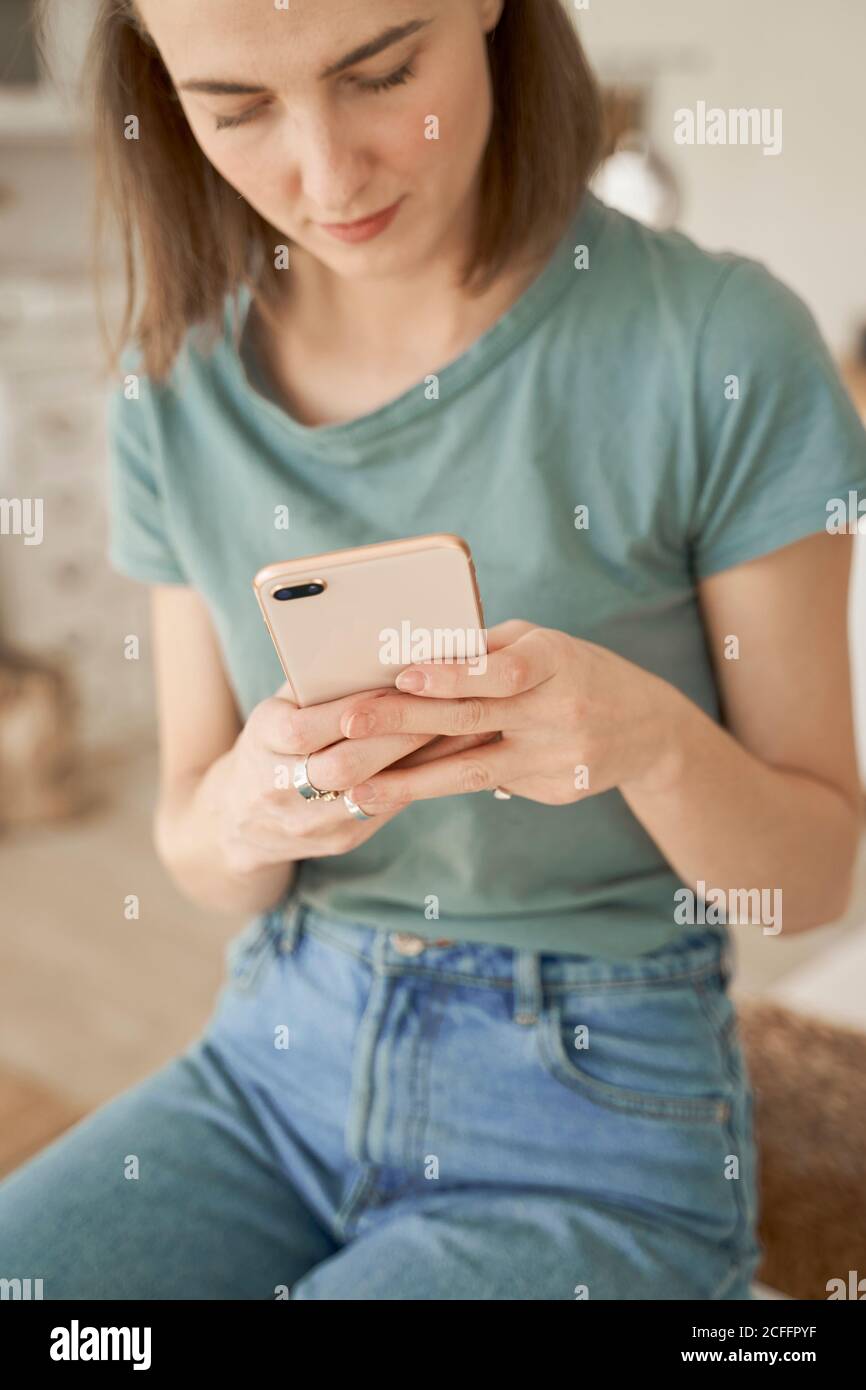 Chilling young barefoot Woman having break and comfortably sitting on white washing machine surfing mobile phone in spacious kitchen Stock Photo