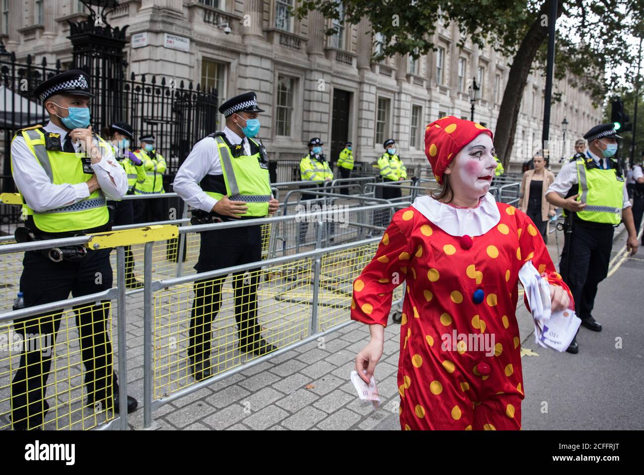 London, UK. 3rd September, 2020. A clown holding banknotes joins fellow climate activists from Extinction Rebellion in front of Downing Street at a ‘Carnival of Corruption’ protest against the government’s facilitation and funding of the fossil fuel industry. Extinction Rebellion activists are attending a series of September Rebellion protests around the UK to call on politicians to back the Climate and Ecological Emergency Bill (CEE Bill) which requires, among other measures, a serious plan to deal with the UK’s share of emissions and to halt critical rises in global temperatures and for ordi Stock Photo