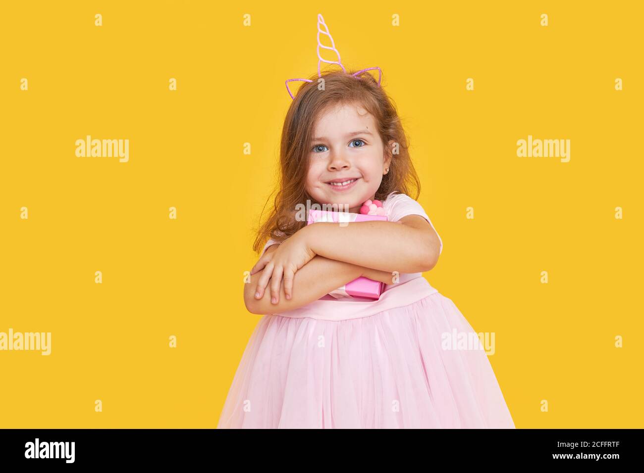 Cute child girl model with wavy hair in elegant pink dress posing on a yellow isolated background. Concept for advertising baby products and holidays Stock Photo