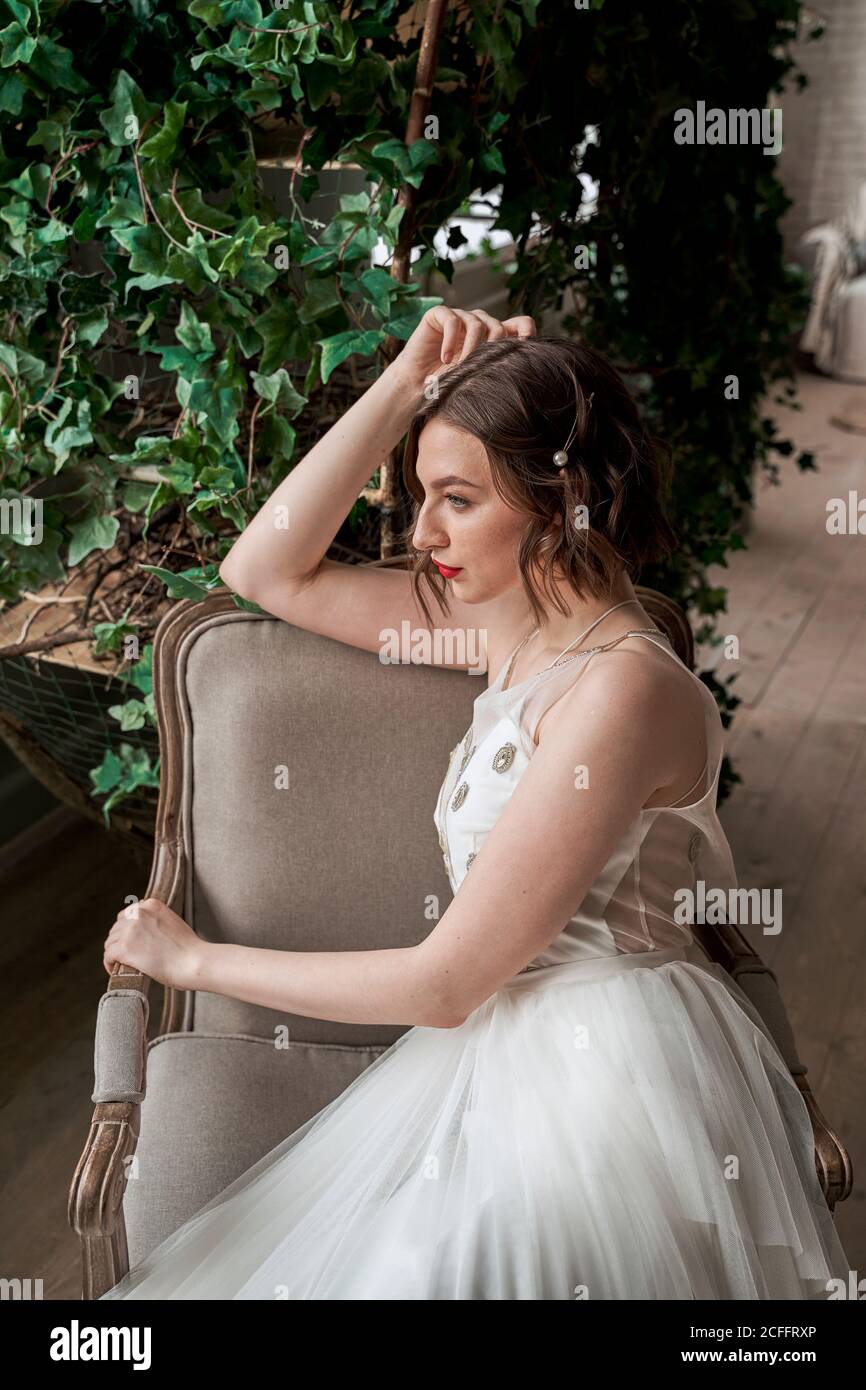 Gorgeous Woman with red lips in white dress sitting on armchair Stock Photo