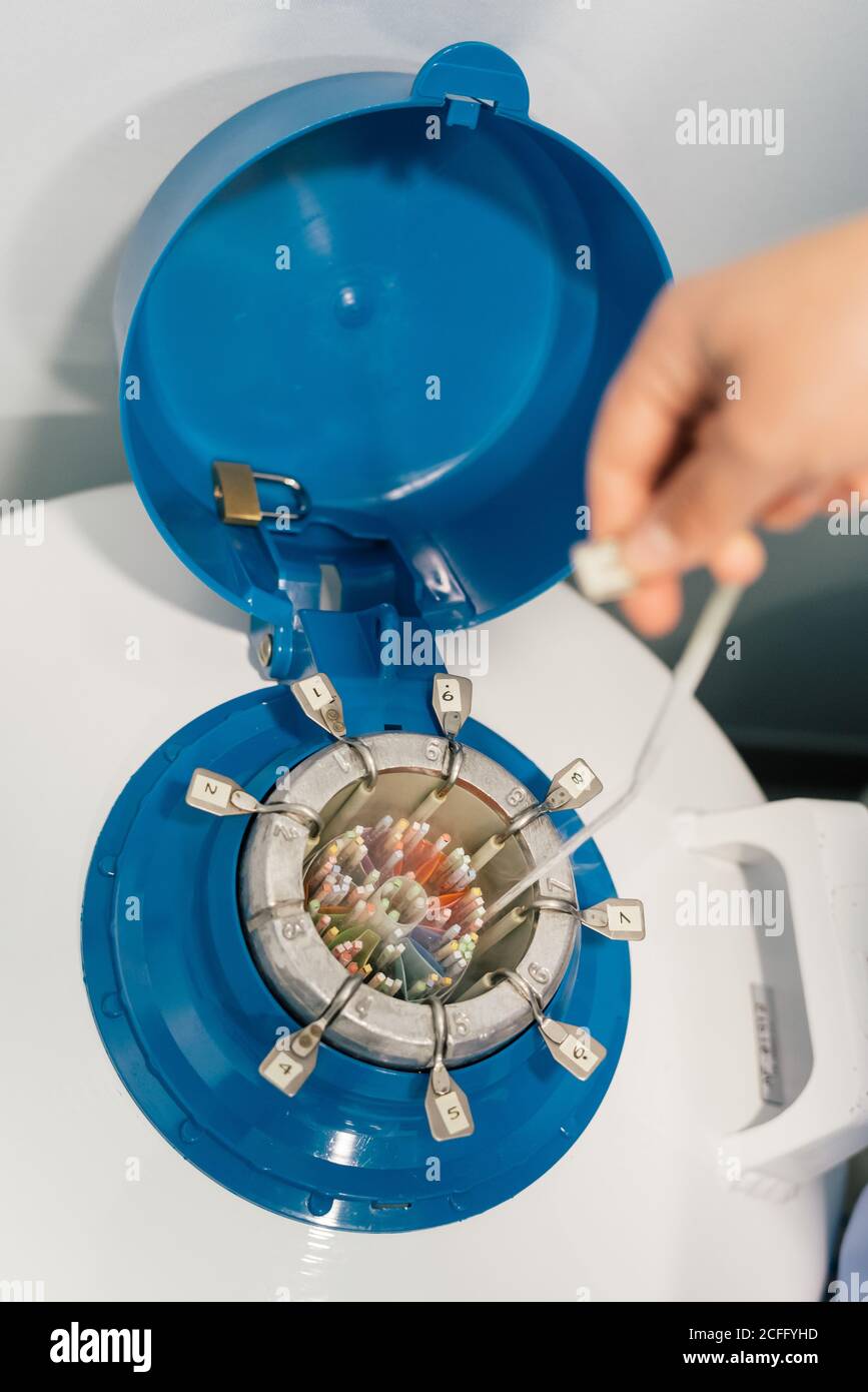 unrecognizable person taking cable with plastic connector from open cryogenic tank with multicolored details and lock on blue lid in laboratory Stock Photo