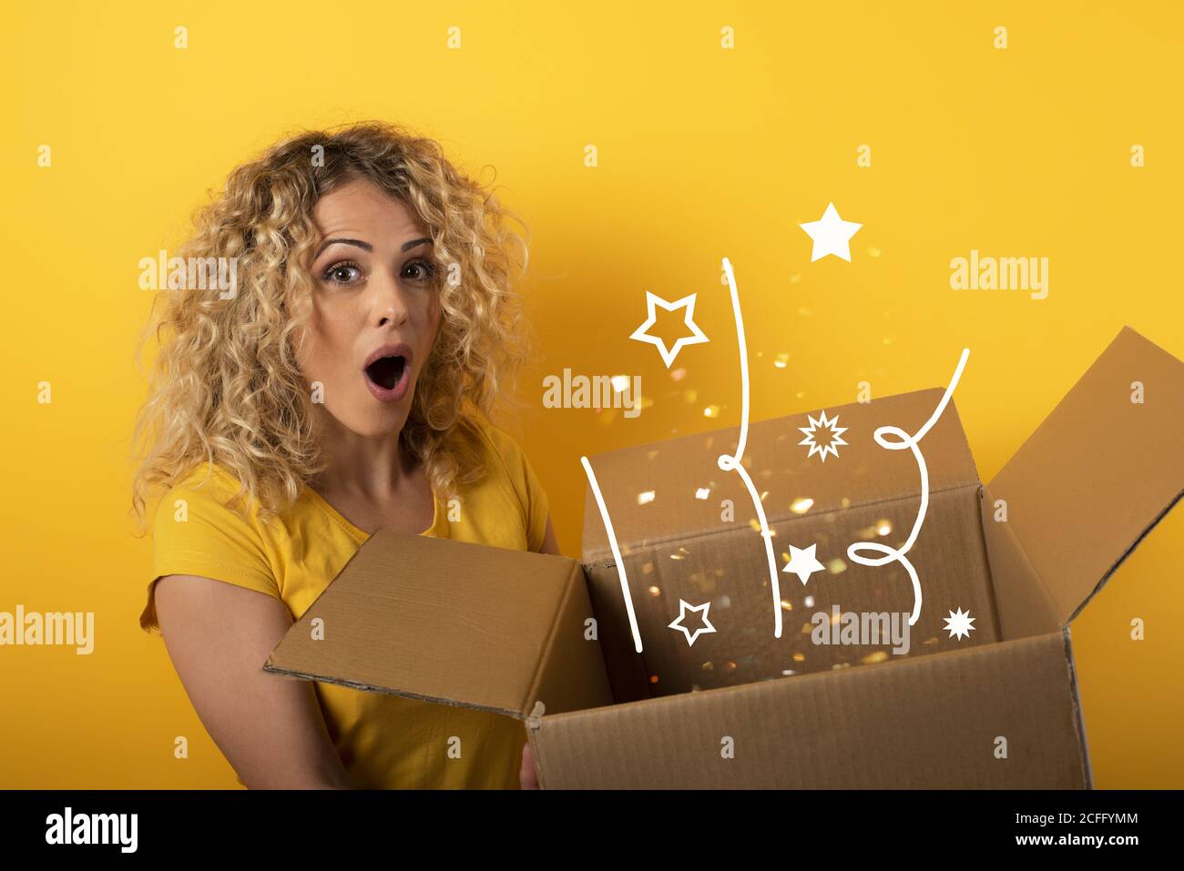 Happy girl receives a package from online shop order. Yellow background. Stock Photo