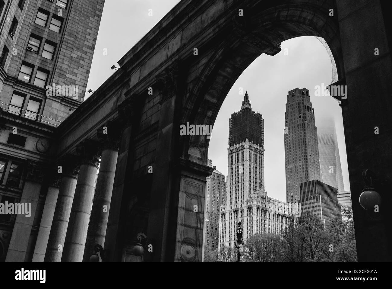 From below of black and white cityscape of Woolworth Building under reconstruction and stone arched passage with columns in Manhattan Stock Photo