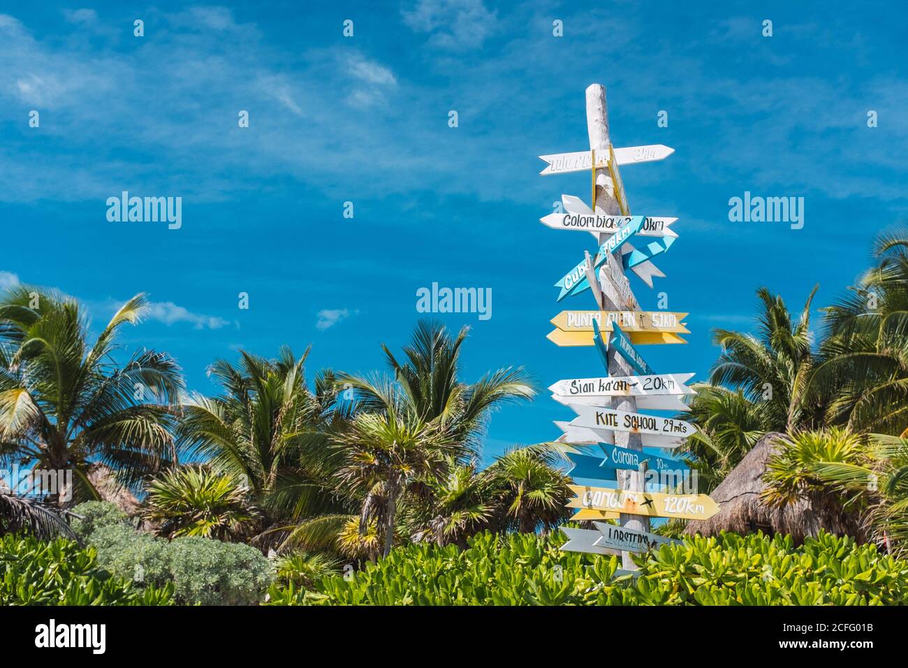 Wooden pole with colorful signboard showing directions to world countries in green palms of Mexico coast Stock Photo