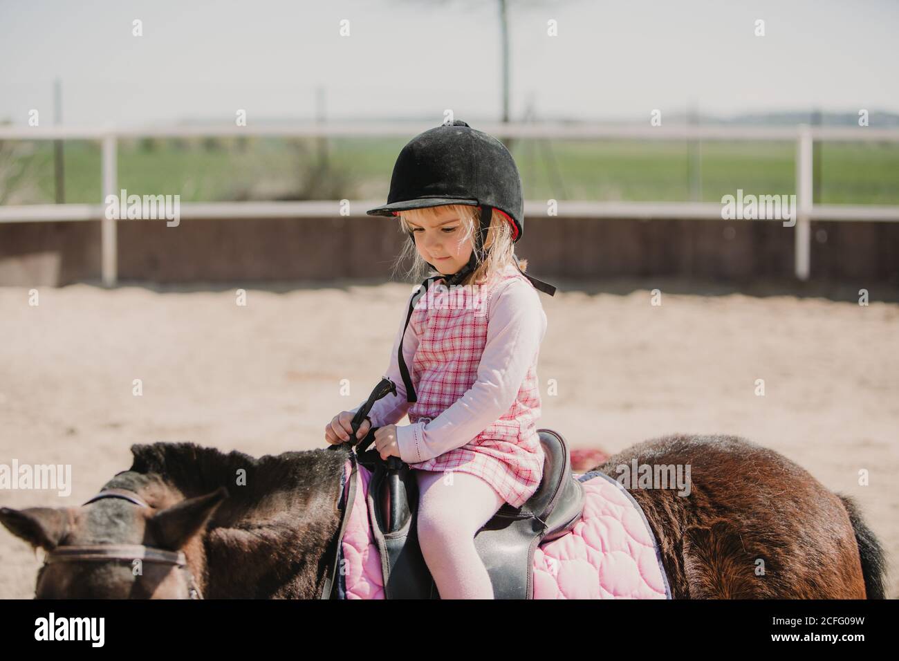 Small girl in dress and jockey hay sitting on horse while learning to