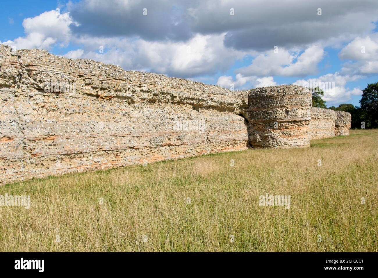 Burgh Castle wall ruins of Roman Fort. Close up view of wall showing construction method and defensive tower. Grass area on the right. Cloudy blue sky Stock Photo