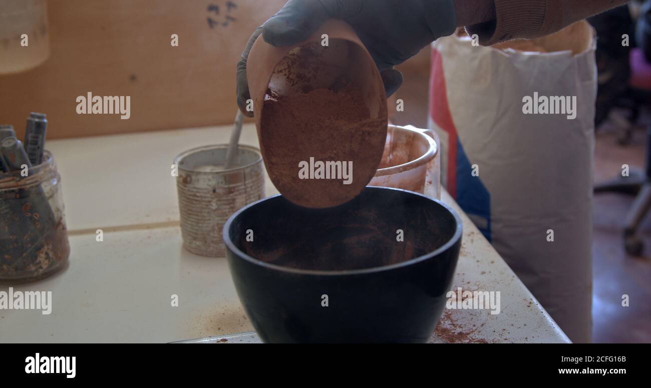 Crop person pouring brown clay into black bowl on table in pottery Stock Photo