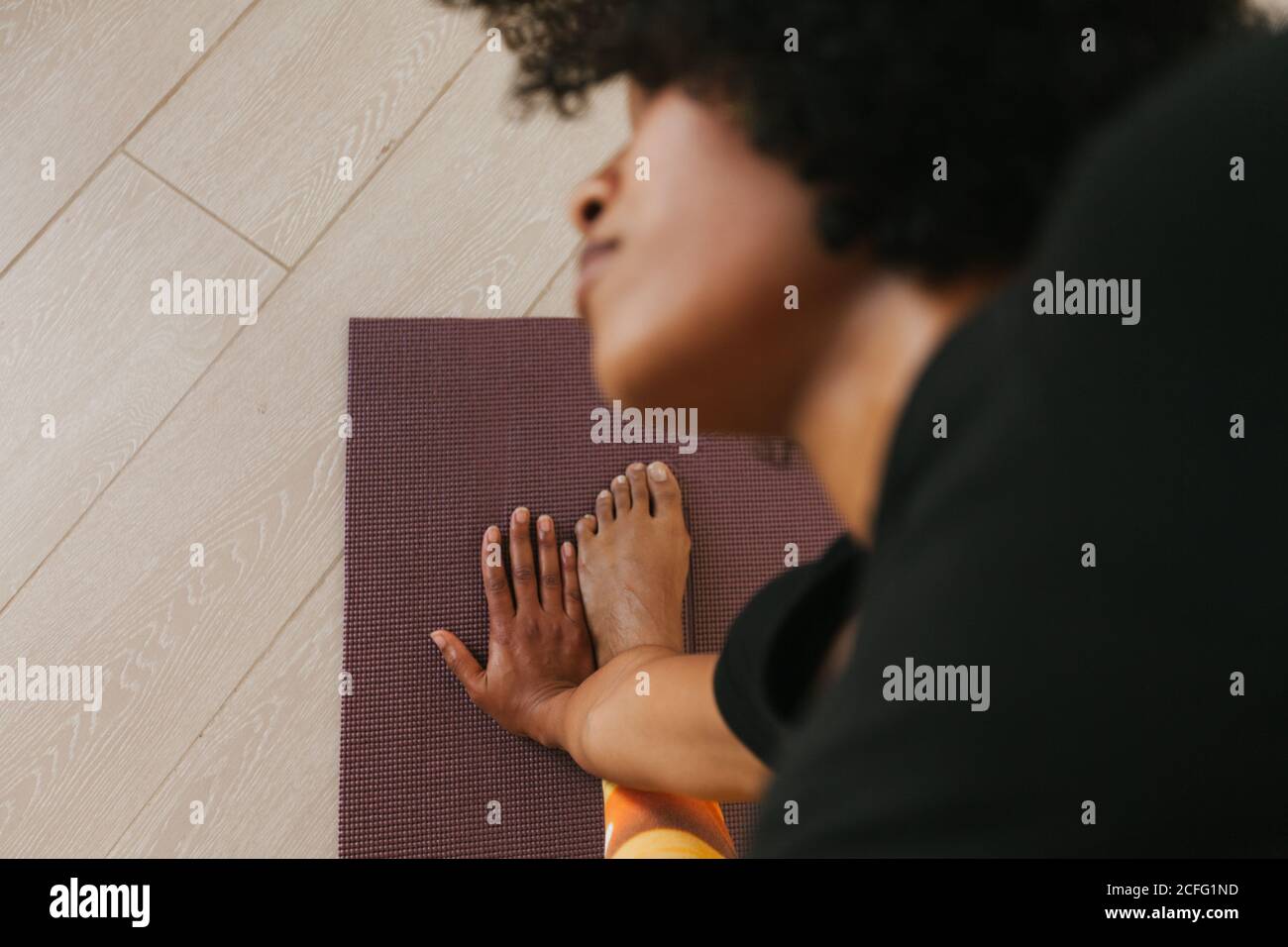 From above close-up view of African American attractive young Woman performing yoga pose with closed eyes on a mat at home Stock Photo