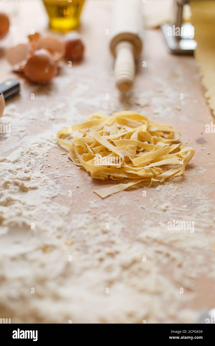 pasta locating on messy wooden table covered with flour with bottle of ...