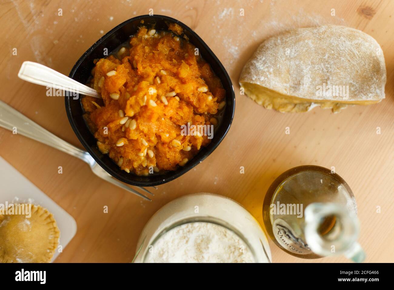 Top view of bowl with delicious filling for ravioli from pumpkin puree and nuts on table near piece of dough olive oil jar of flour and cutting board with raw ravioli Stock Photo