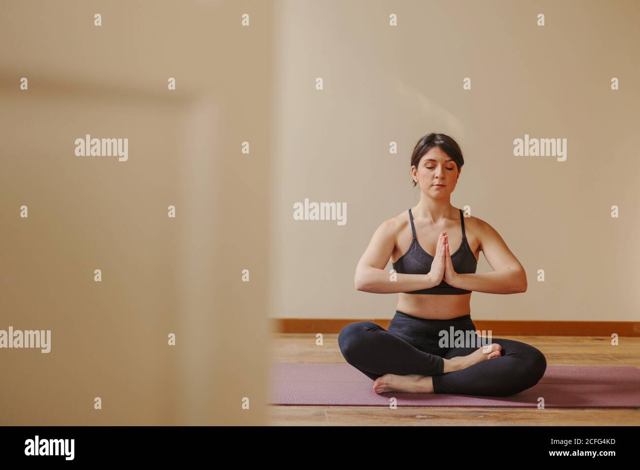 Female sitting on mat with closed eyes and Namaste gesture while practicing mindfulness in Padmasana at home Stock Photo