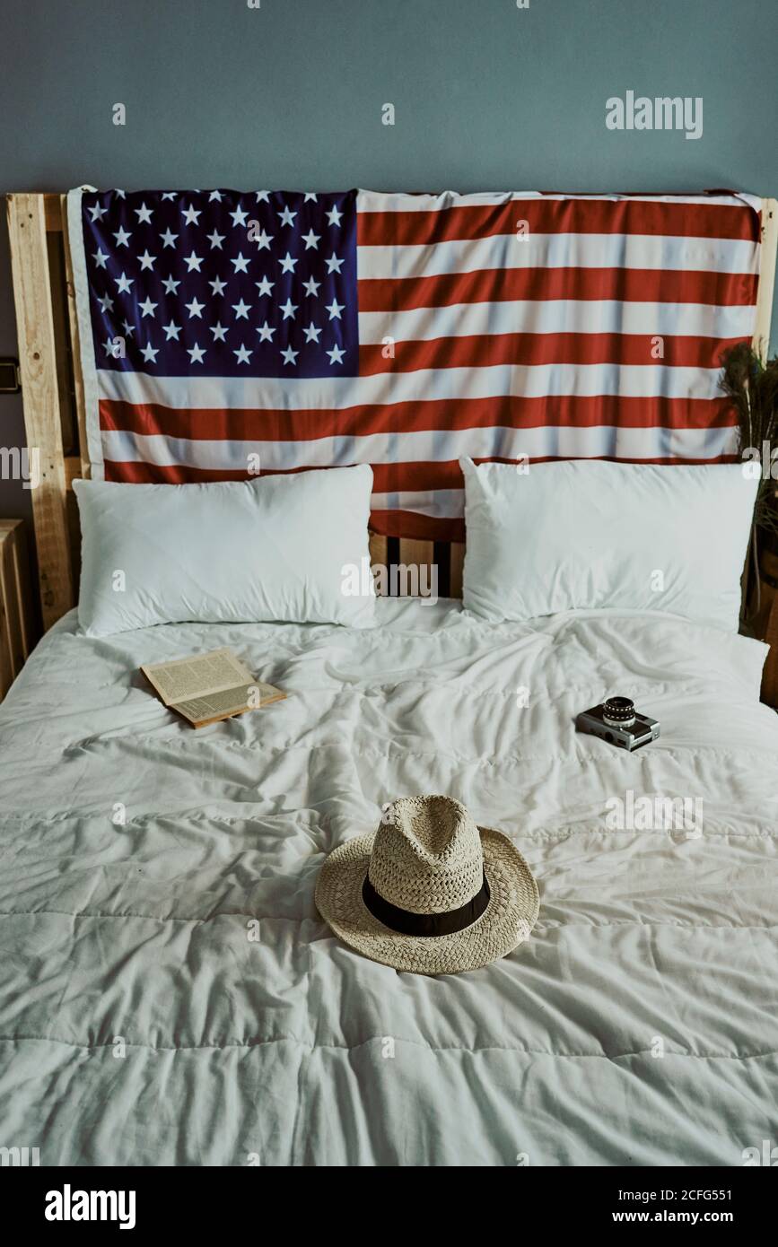 A bed with a hat, a book and a camera with the American flag on the headboard Stock Photo