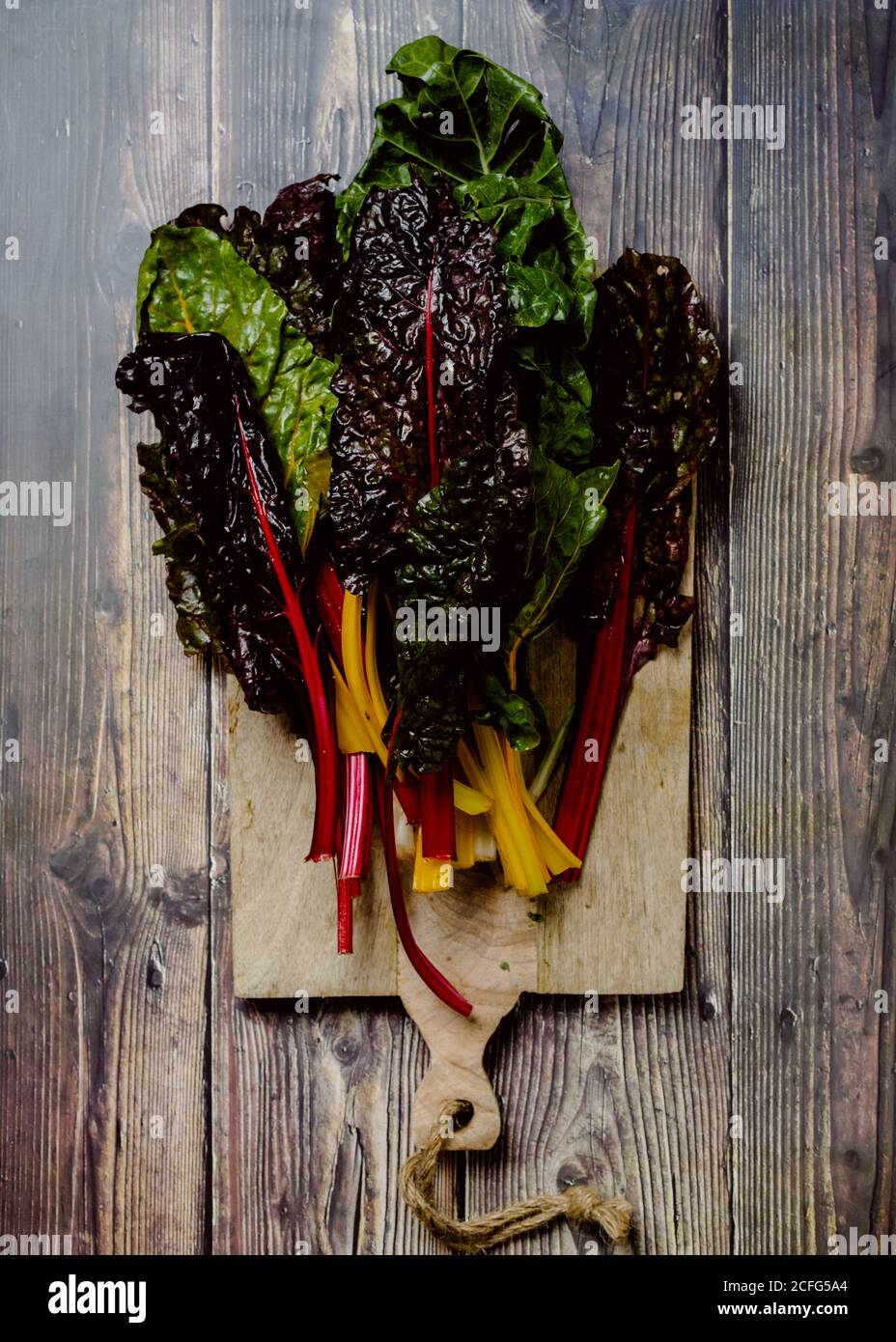 Bunch of vivid varicolored fresh foliage of edible herbs and vegetables over wooden cutting board placed on old rustic table Stock Photo