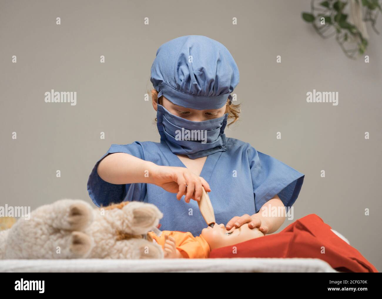 young child wearing medical PPE examines a baby doll by checking it's temperature with thermometer Stock Photo